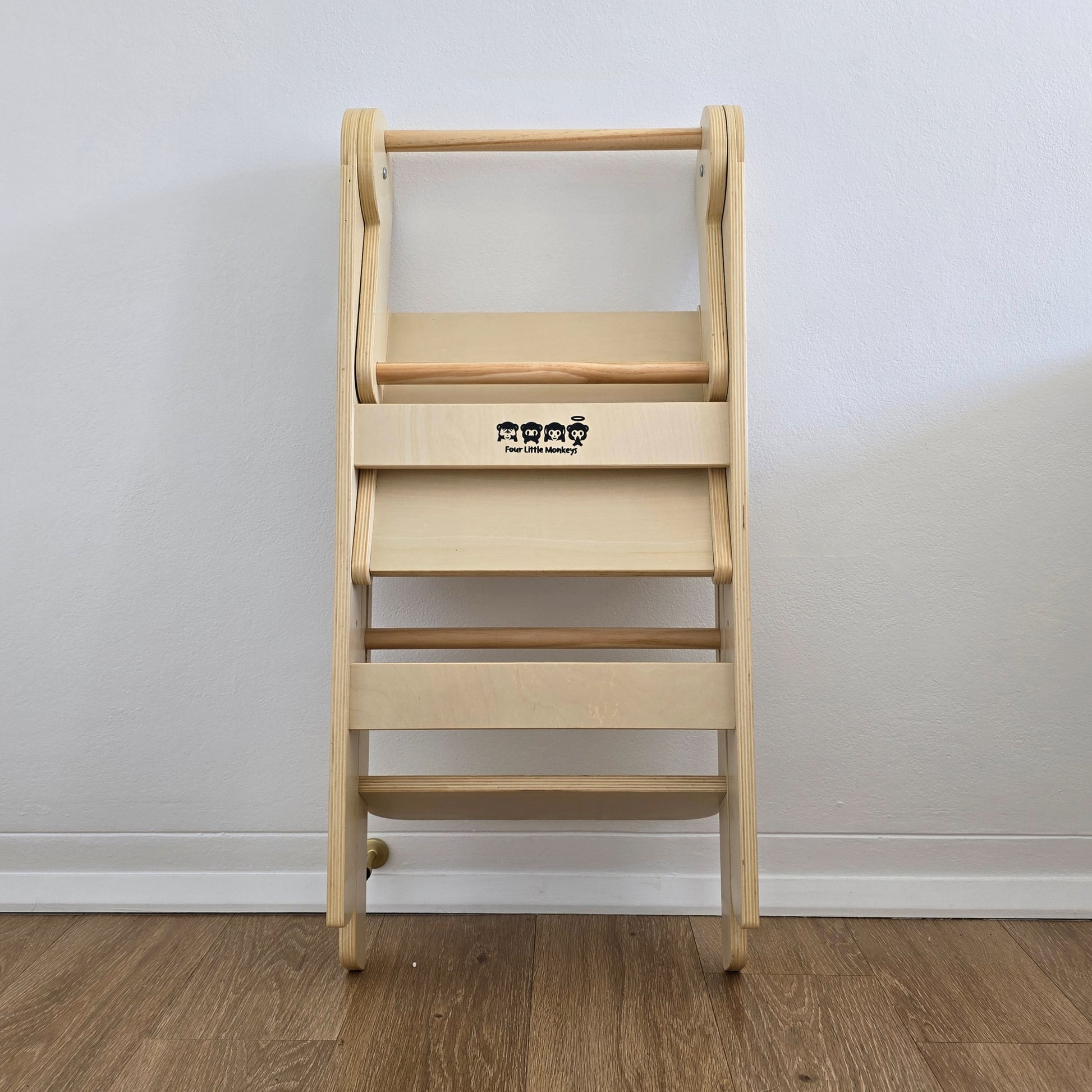 Four Little Monkeys Natural Adjustable Foldable Learning Tower folded up and leaning against a wall for easy storage.