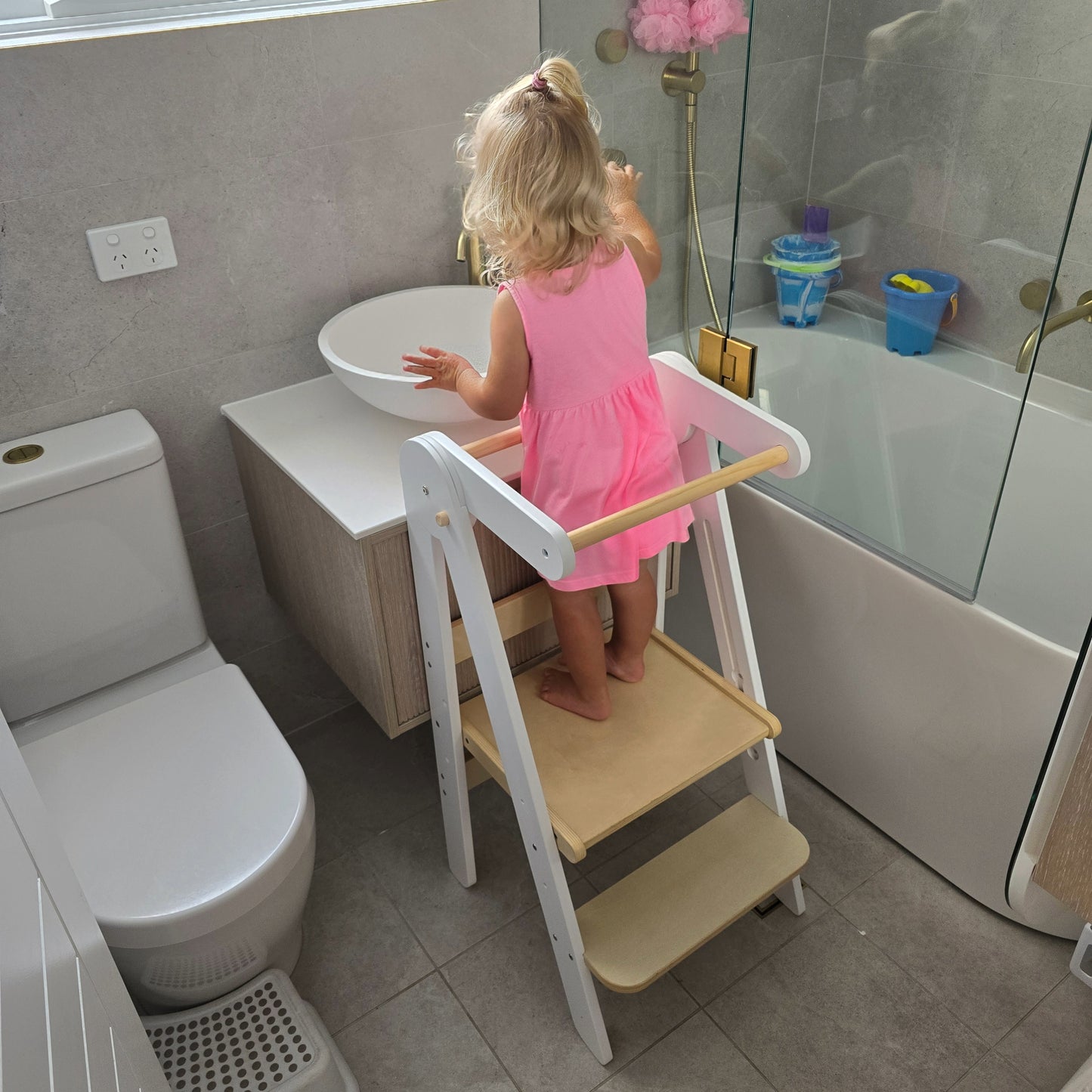 Toddler on the Four Little Monkeys White Adjustable Foldable Learning Tower reaching bathroom sink to wash their hands