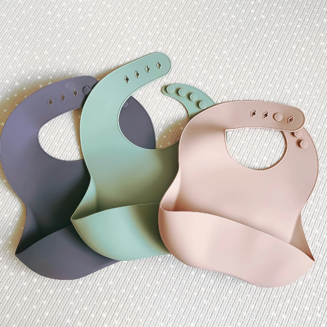 Image of a silicone bibs in a range of 3 colours, grey, sage green and warm taupe with the brand name 'Four Little Monkeys'.