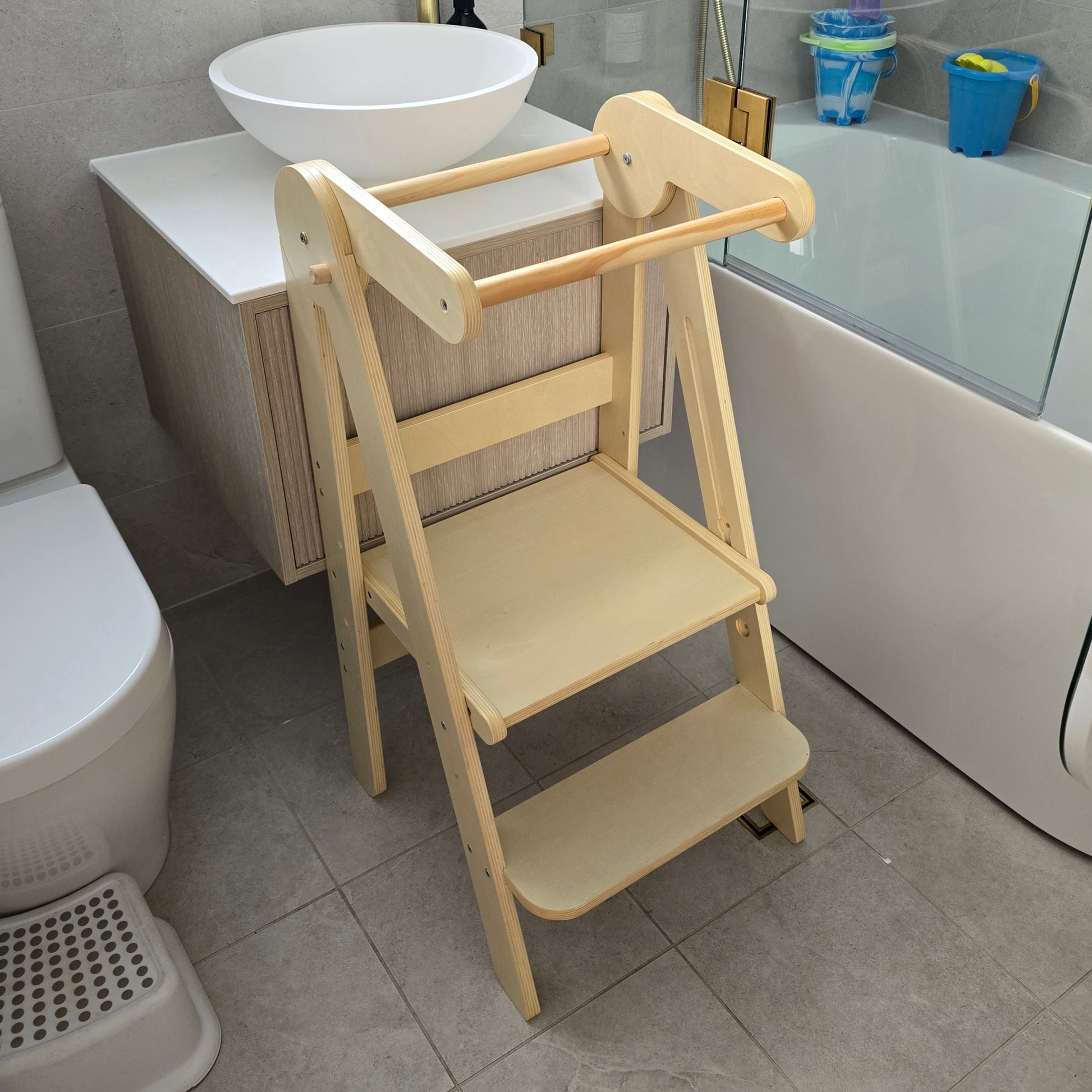 Four Little Monkeys Natural Adjustable Foldable Learning Tower in position at a bathroom sink, ready for a child's use.
