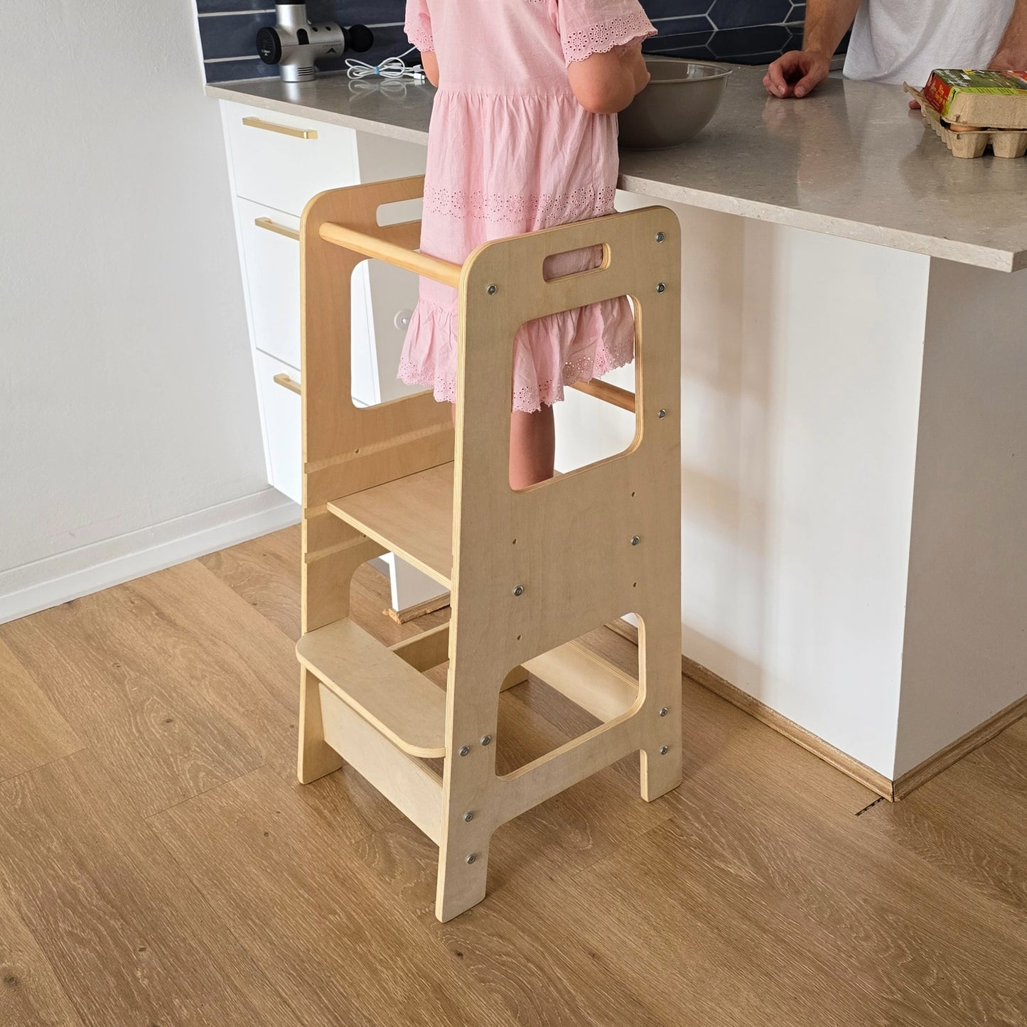 Little girl standing on an Adjustable Learning Tower at a kitchen breakfast bar helping her father in the kitchen.