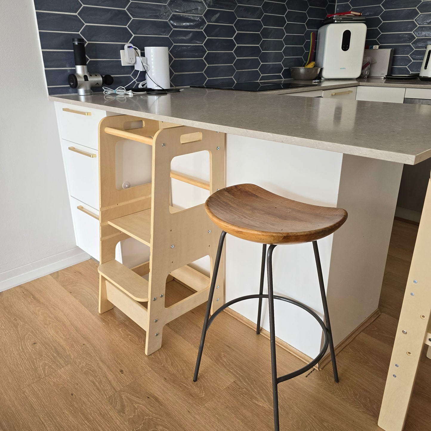 The Natural Adjustable Learning Tower neatly tucked under a kitchen breakfast bar.