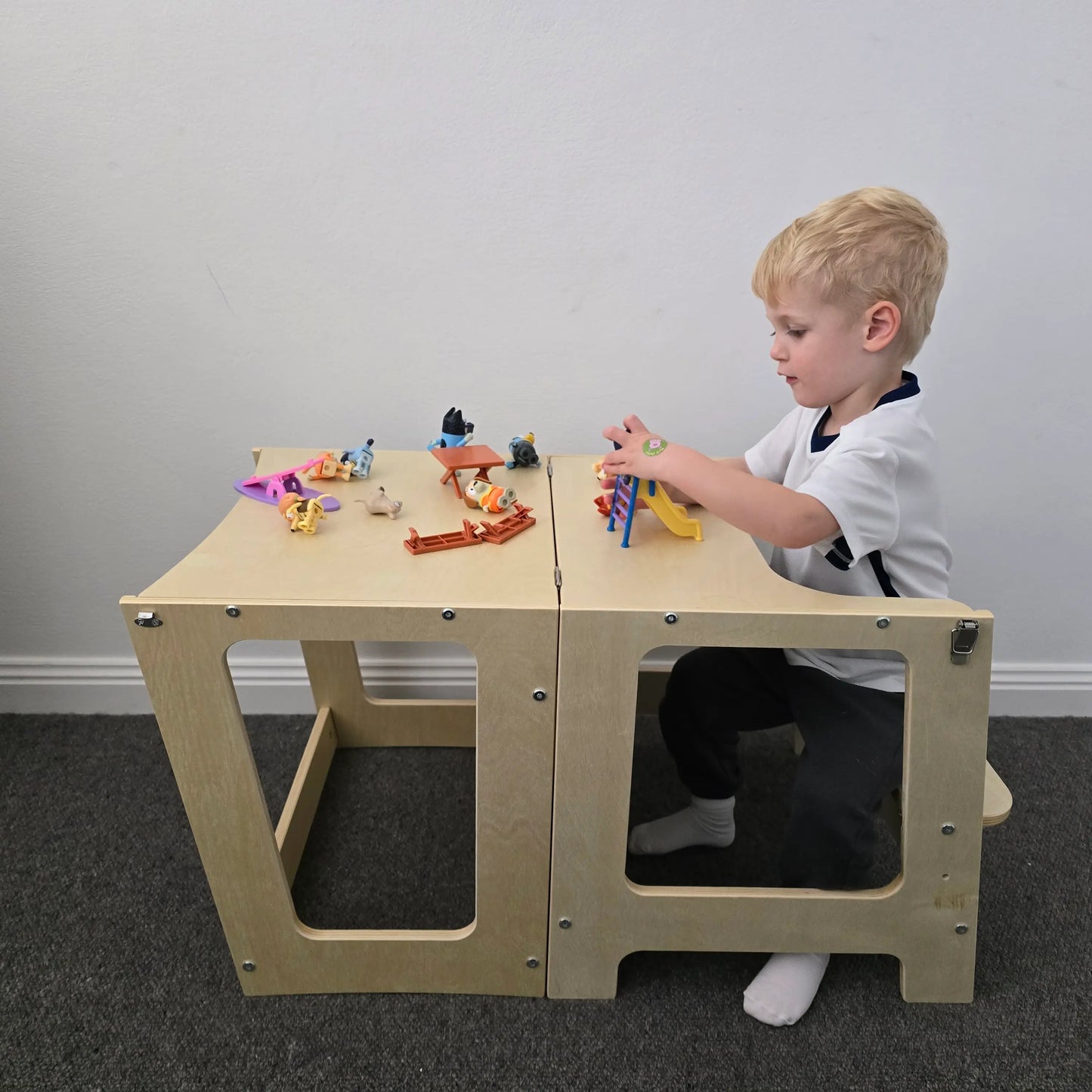A young child playing on the wooden convertible learning tower set up as a table, with the child engaged in an activity on the tabletop.