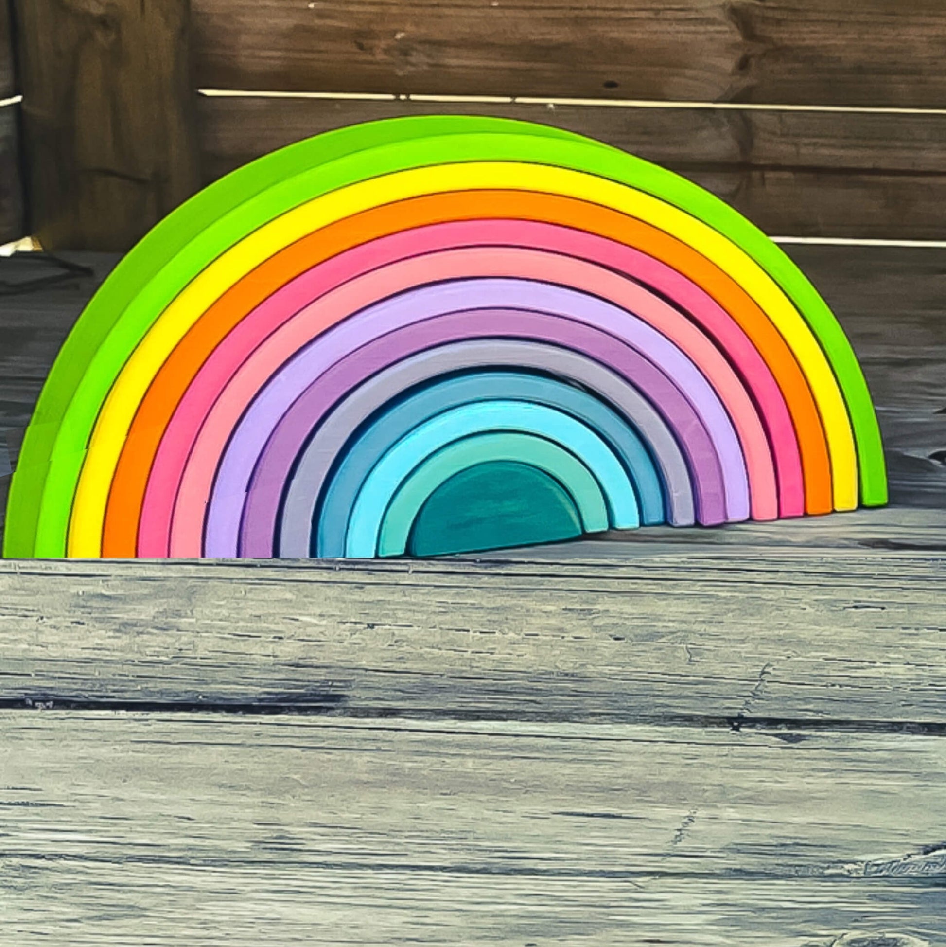 An image showing a front view of a pastel rainbow arch Montessori toy. The toy is made up of wooden arched blocks in various pastel colors, arranged in a curved formation. The Montessori toy promotes open-ended play and encourages color recognition and fine motor skills development.