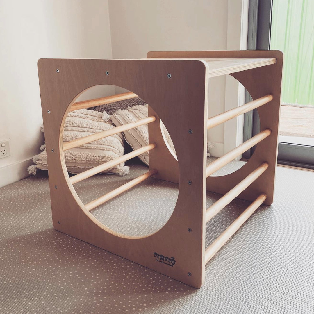 An image showcasing the Pikler cube, a versatile wooden climbing structure for children. It features various platforms and bars, promoting gross motor development and imaginative play.