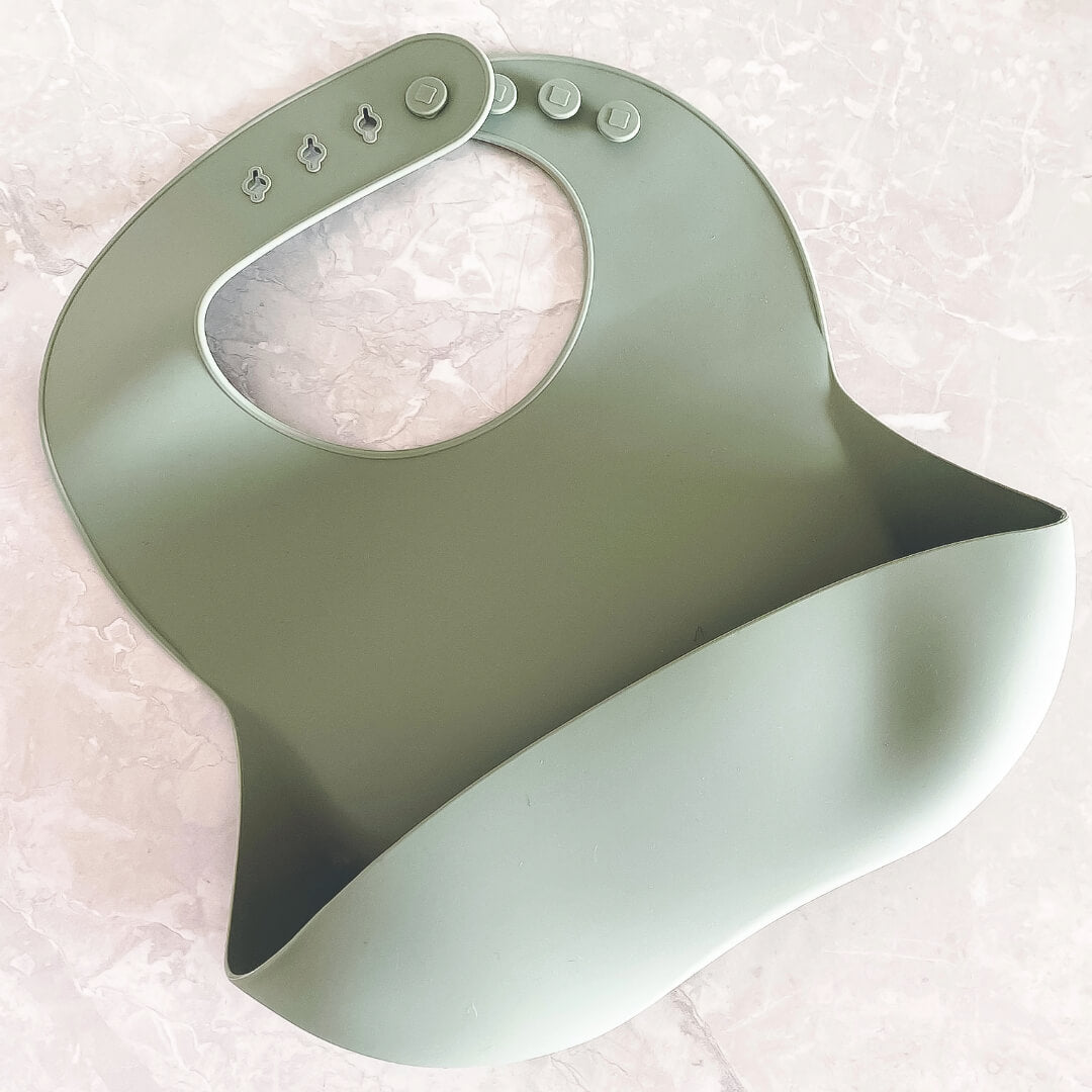 Image of a sage green silicone bib with the brand name 'Four Little Monkeys'