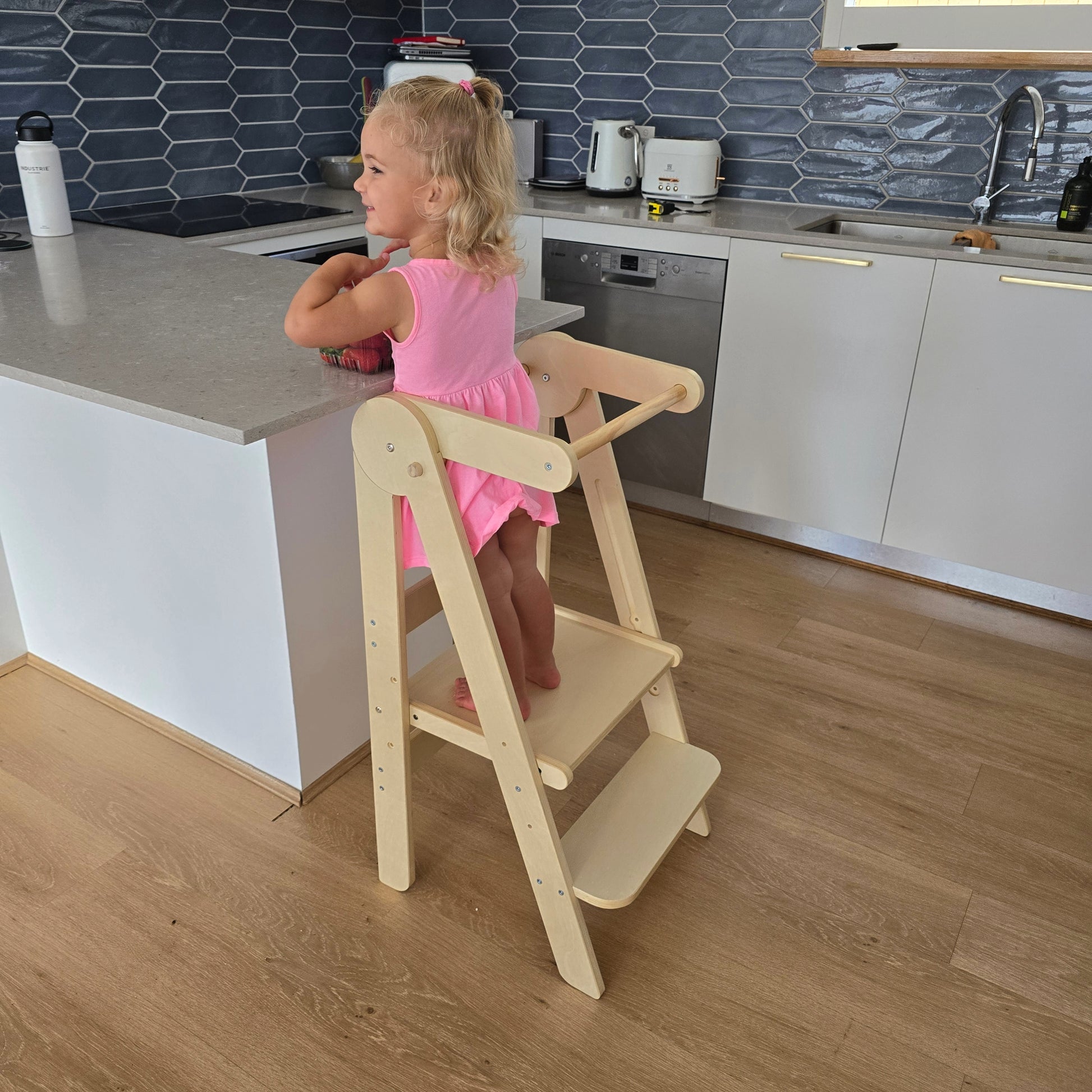 Toddler on the Four Little Monkeys Natural Adjustable Foldable Learning Tower reaching kitchen countertop, enhancing engagement during meal prep.